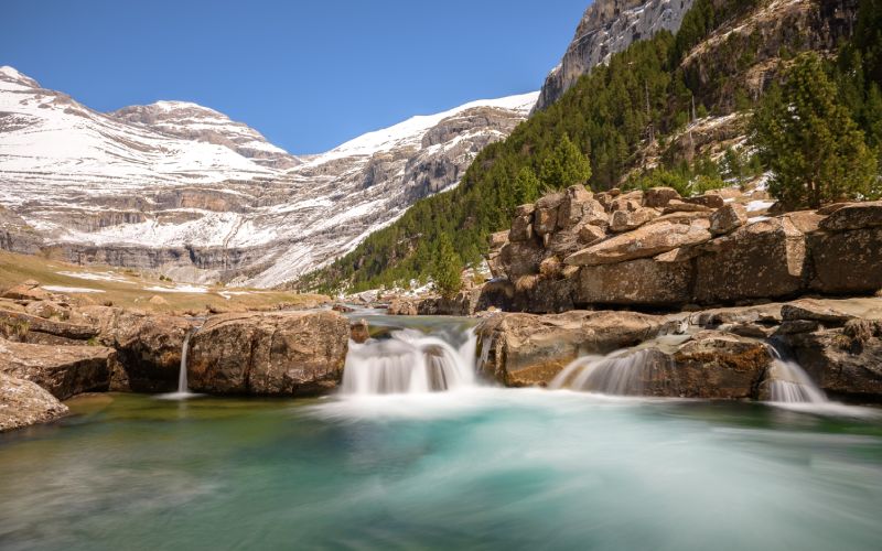 Vista de una caída de agua en el río Ara, en el Parque de Ordesa y Monte Perdido, con las montañas nevadas al fondo