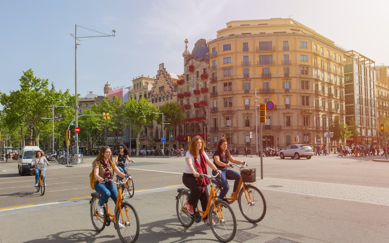 Some girls riding bikes next to Batlló house in Barcelona.
