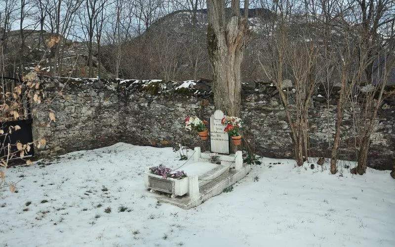 A solitary tombstone in an empty graveyard, with flowers and covered in snow