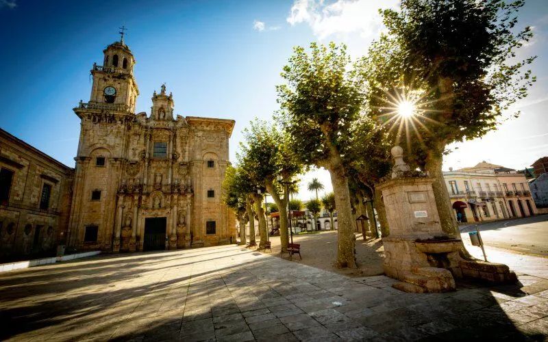 An old square with some trees, a fountain and a monastery
