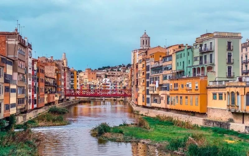 The view of a river crossed by a red bridge, colourful houses on both sides