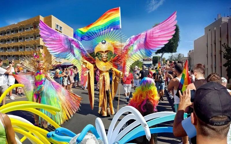 A colourful parade, and someone with wings and the rainbow flag in the middle