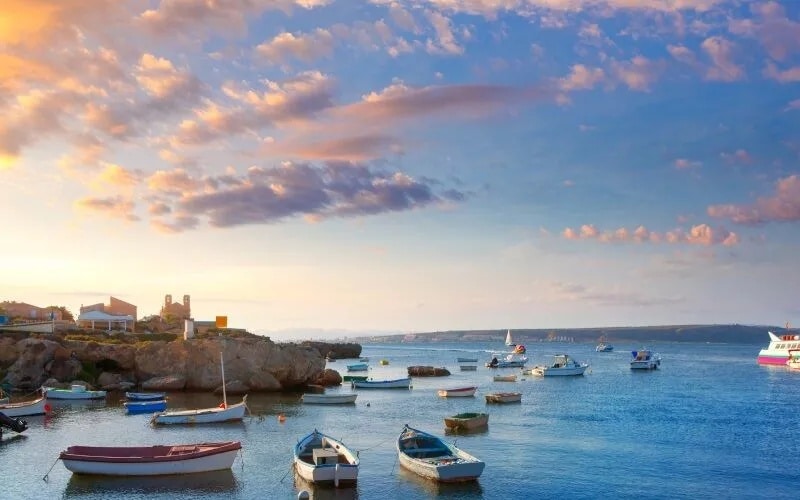 A harbour with boats and a colourful sky crossed by sparse clouds