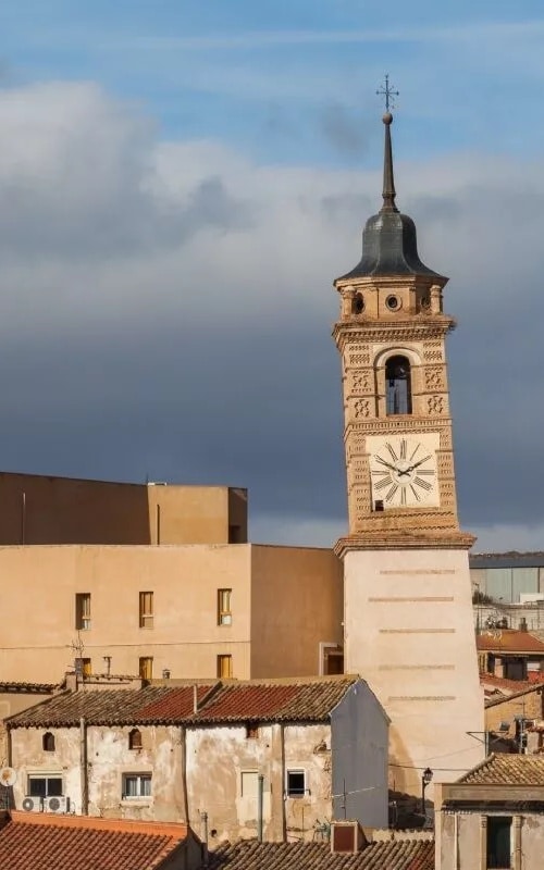 A leaning tower next to a church, with small old houses around it
