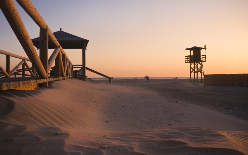 A beach at sunset, with a wooden structure