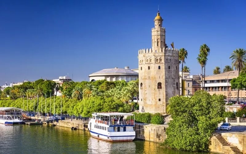 A tower next to the river with a few boats and palm trees