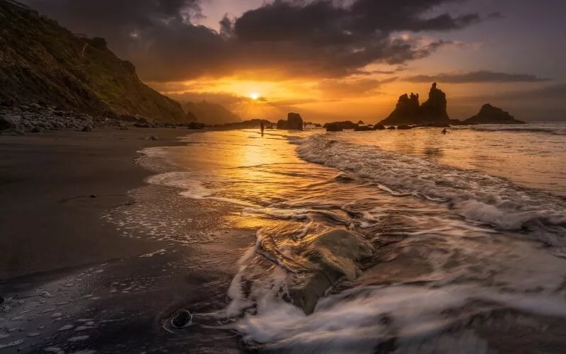 A sunset on a beach with dark sands