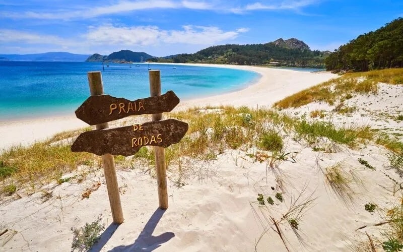 A wooden signal on the sand and the beach in the background