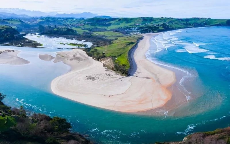 A panoramic view of a white beach surrounded by green hills