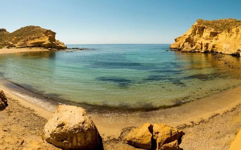 A beach with yellow-coloured rocks around it