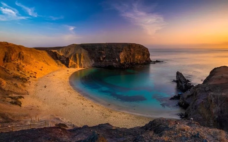 A panoramic view of a turquoise beach surrounded by reddish rocks and land