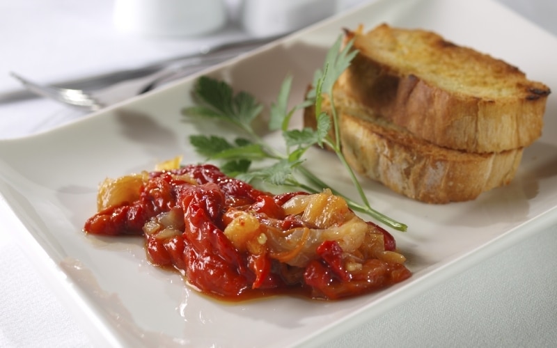 A red pepper dish on a white plate, with some bread on the side