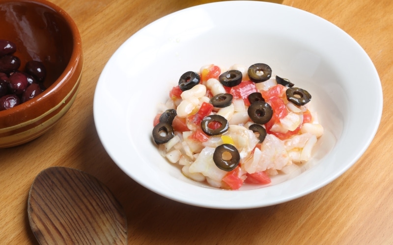 A salad with white beans and olives on a white plate 