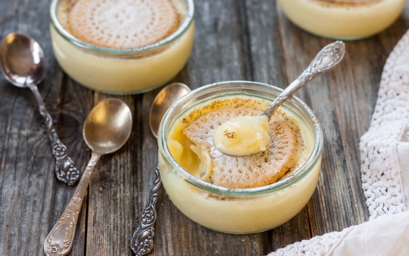 Three cups of custard with biscuits and teaspoons on the table