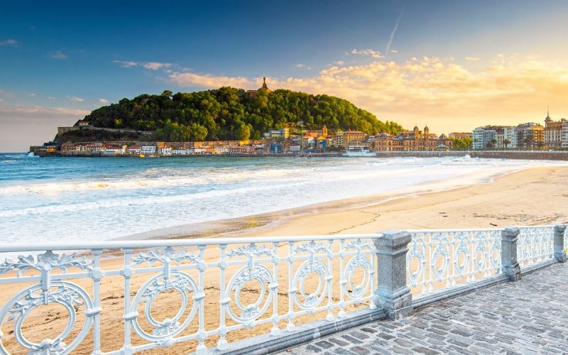 A beautiful beach with a white railing in front and a mountain in the distance