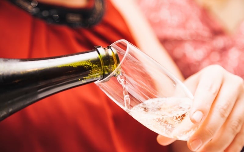 A person with a red dress pouring a glass of sparkling wine
