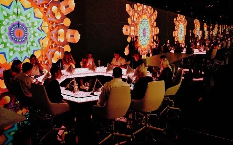 A table with people in it and screens with colours and shapes in an expensive restaurant