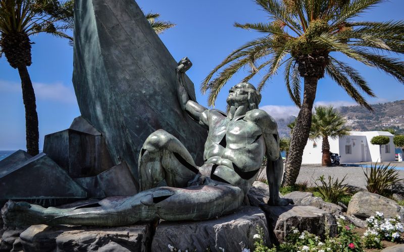 A bronze statue of a man sitting next to a ship
