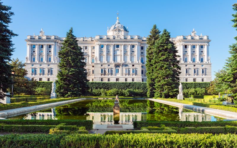 Front view of the Royal Palace of Madrid with a pond and pine trees