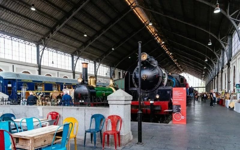 A train surrounded by stalls and some colourful chairs in front