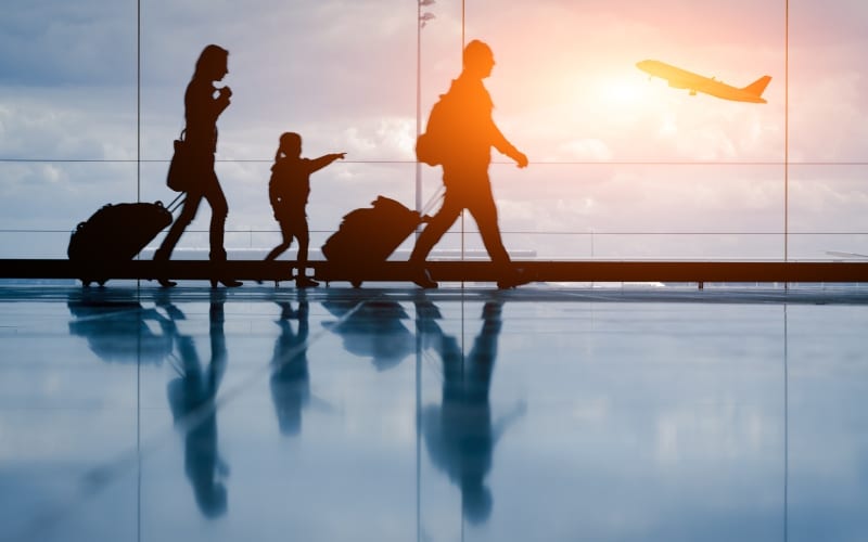 A family walking through an airport with a plane on the other side of the window