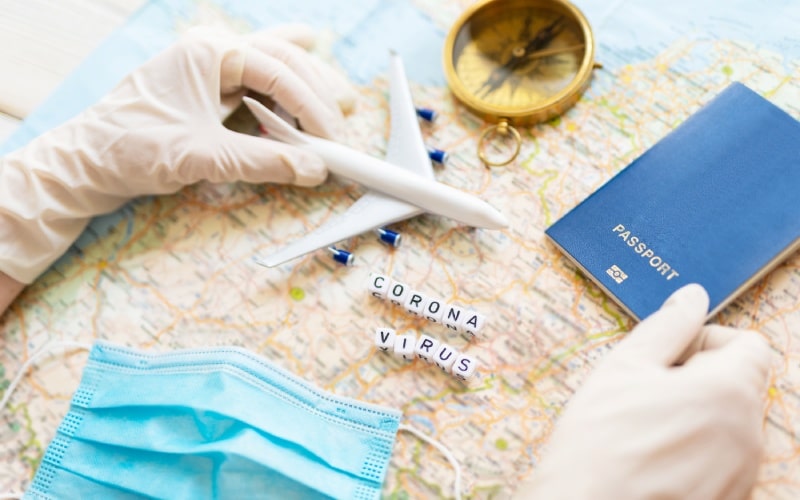 Two gloved hands on a map with a passport, a toy plane, a compass and a mask